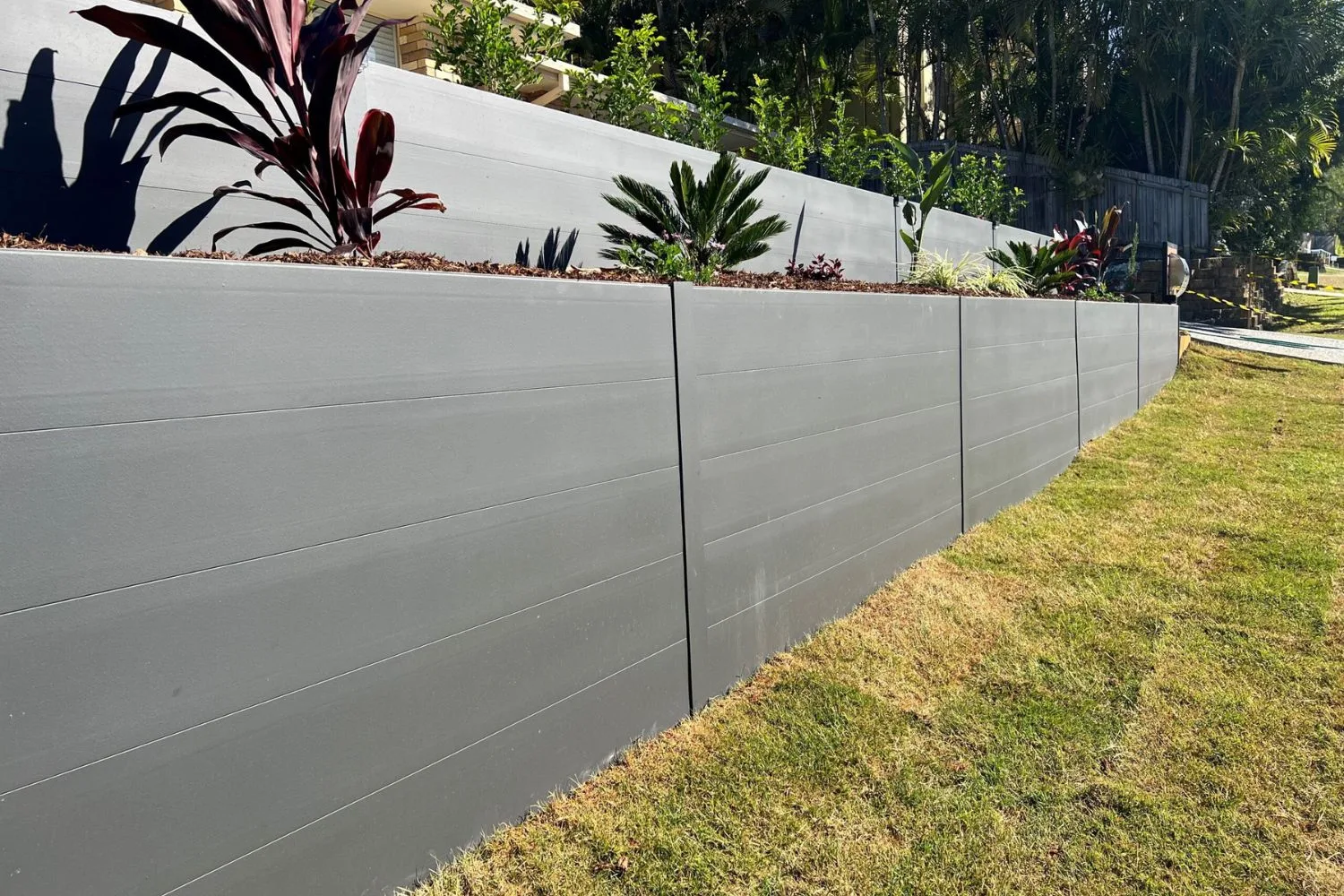 A grey concrete sleeper retaining wall with tropical planting