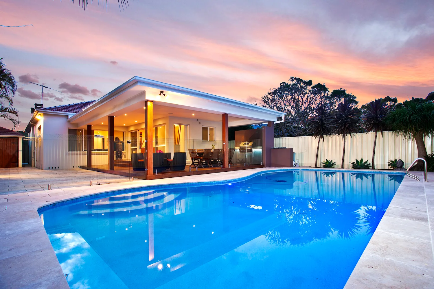 A backyard pool and covered outdoor living pavilion at dusk
